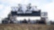Aufblasbares Wacken Open Air Logo auf großem, schwarzen Container über dem Eingang zum Festivalgelände mit anstehenden Menschen.