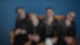 Royal Republic sitzen auf deinem gelb-braunen Samt-Sofa vor einer knallblauen Ziegelsteinmauer
